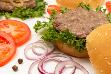 Burger bun on lettuce leaf. Chopped tomatoes and onions on table