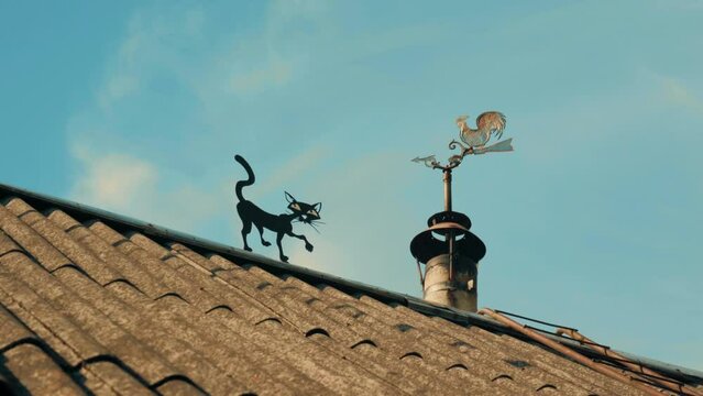 the roof of a house in the village, on which a weather vane in the form of a rooster is spinning near the chimney, to which a cat is sneaking