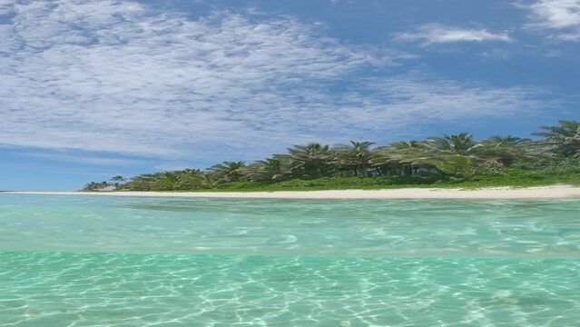 VERTICAL SLOW MOTION, HALF UNDERWATER: Summer sun shines on tranquil turquoise ocean and stunning tropical beach surrounded by lush palm trees. Cool shot of empty exotic island beach in low season.
