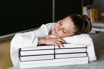 Tired schoolgirl lies and sleeping on books at blackboard in school. School education. The girl is tired of teaching homework.
