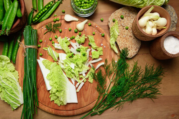 vegetables on a wooden kitchen board, green onions, dill and peas, sliced cabbage on a wood...