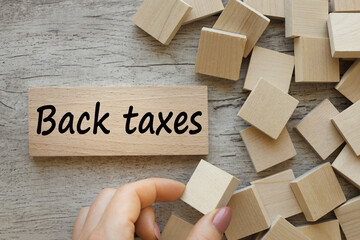 back taxes on a beautiful wood background. a woman's hand holds a wooden block with text.