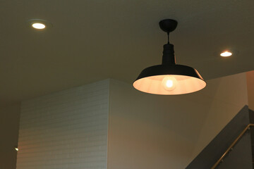 Illumination of an iron pendant lamp shade with a simple design hung in a dimly lit room
