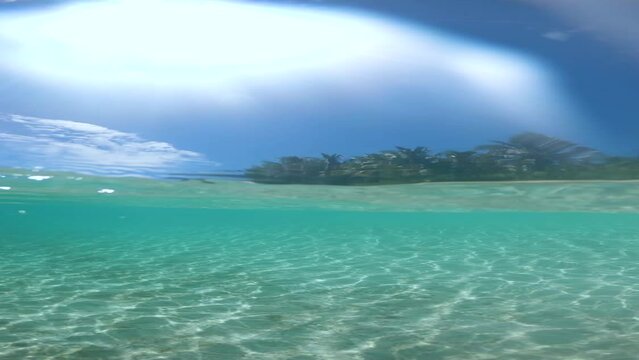 VERTICAL SLOW MOTION, HALF UNDERWATER, LENS FLARE: Bright summer sunbeams shine on empty white sand beach and tranquil ocean near French Polynesia. Awesome shot of remote sandy shore on hot summer day