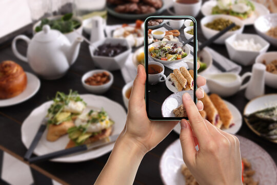 Woman taking picture of different dishes served on wooden table, closeup