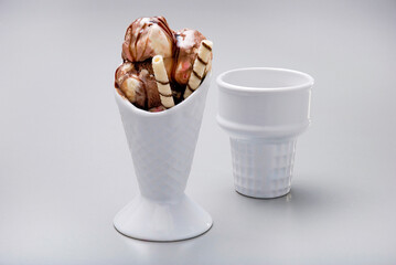Two white ceramic ice cream cones, one of them has scoops of neapolitan ice cream, isolated on white