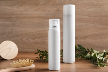 Dry shampoo sprays, green leaves and hairbrush on wooden table