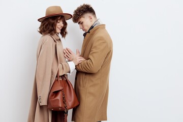 a happy couple in love is standing in beige stylish autumn coats on a white background and a man is holding a woman's hands smiling pleasantly