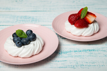 Pavlova cake with strawberries and blueberries and mint on a pink platter. Home confectionery. Old retro white and blue table.