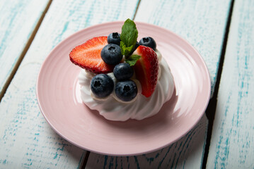 Pavlova cake with strawberries and blueberries and mint on a pink platter. Home confectionery. Old retro white and blue table.
