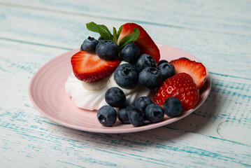 Pavlova cake with strawberries and blueberries and mint on a pink platter. Home confectionery. Old retro white and blue table.