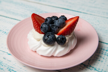 Pavlova cake with strawberries and blueberries on a pink platter. Home confectionery. Old retro white and blue table.
