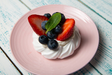 Pavlova cake with strawberries and blueberries and mint on a pink platter. Home confectionery. Old retro white and blue table.