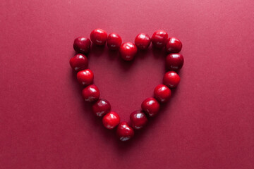 Ripe cherries laid out in the shape of a heart. Red background with space for text. Top view. Food concept. Copy space