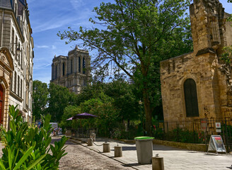 Fototapeta na wymiar Paris, France. June 2022. The beauty of Notre Dame peeping through the trees in a side street of the Latin Quarter. Beautiful summer day.