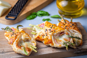 Baked green asparagus with ham and cheese in puff pastry sprinkled with sesame seeds and green basil leaves.