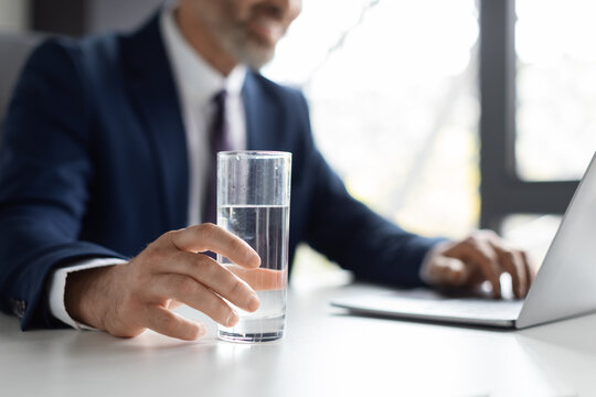 Unrecognizable Middle Aged Businessman Holding Glass Of Water While Sitting In Office