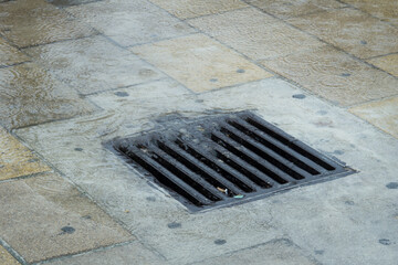 Water during a rainstorm flows into the drainage grate. Rainwater flowing down the impervious pavement to the storm drain equipped with cast iron grid during a rain.