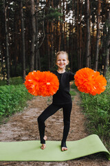 A beautiful, smiling girl, a child cheerleader in a black suit dances, performing movements, in the...