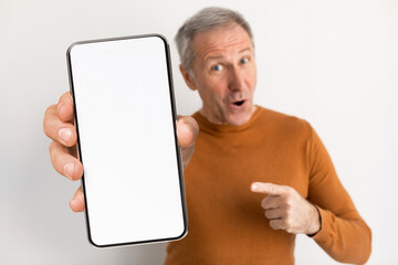 Online Offer. Excited Senior Man Pointing At Big Blank Smartphone In Hand