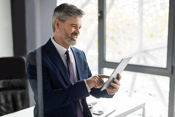 Successful Mature Businessman Using Digital Tablet At Workplace In Office