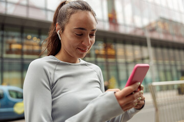 Young healthy sporty woman using cell phone during rest after jog