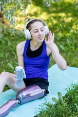 Young beautiful athletic woman with bionic prosthetic leg doing sport exercises in the park...