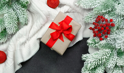Christmas card knitted plaid white gift box with a red bow and fir branches in the snow.