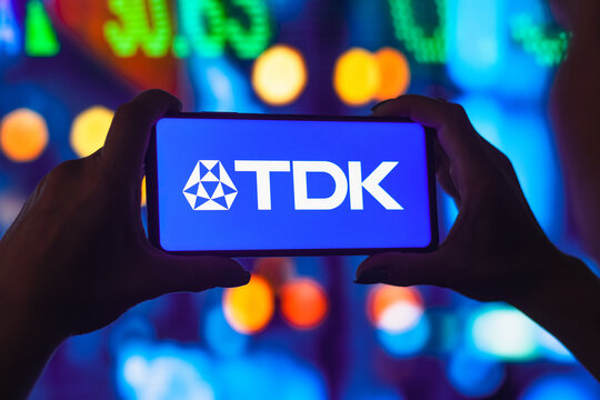 July 11, 2022, Brazil. In this photo illustration, a silhouetted woman holds a smartphone with the TDK Corporation logo displayed on the screen.