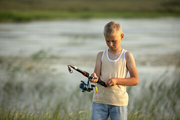 Little boy is fishing at sunset on the lake