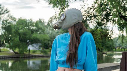 Girl with long hair in a gas mask on the river bank. Alienation in the city. Fashion, ecology and...