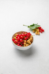 Currant berries with green leaves in white bowl on light background. Red and white currants. Selective focus.