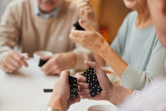 Close-up of unrecognizable senior man looking at domino pieces and thinking of strategy while playing dominoes with friends