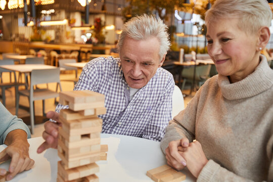 Group of concentrated senior friends sitting at table in nursing home leisure room and playing jenga