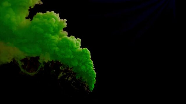 Colorful green smoke bomb or haze grenade blowing across screen for festival or celebrations on black background.