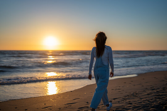 woman dressed in a denim jumpsuit walking on the beach at sunset