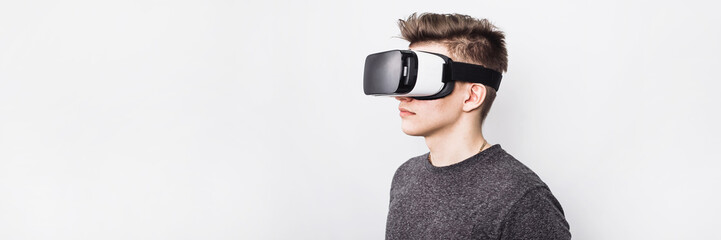 A young guy, a teenager stands in a villard vr glasses on a white background. Augmented reality in...