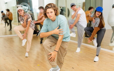 Portrait of cheerful teenage boy practicing hip-hop movements during group dance lesson in studio.