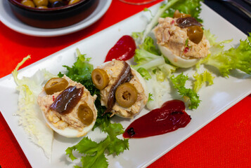 Boiled stuffed eggs with cheese filling and olives, served with lettuce and tomatoe sause