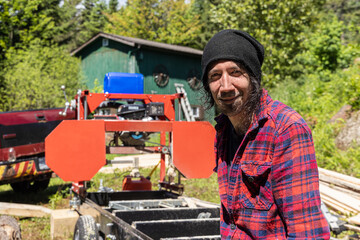 Fototapeta na wymiar Close up portrait of a male lumberjack in mid thirties at work outdoors. Blurry machinery and cabin is seen in background with copy space to left.
