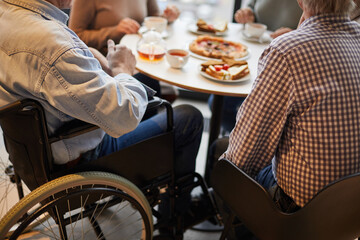 Close-up of unrecognizable handicapped man in wheelchair surrounded by friends sitting at table and chatting with friends