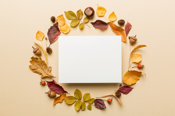 Fototapeta premium Autumn composition with paper blank and dried leaves on table. Flat lay, top view, copy space