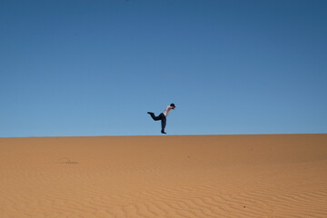 Man jumps over the sand dunes. Colorful wide shot of a funny moment in a desertic landscape 