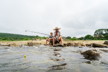 Grandfather fisher in straw hat and little male grandkid enjoying leisure activity use fishing rod