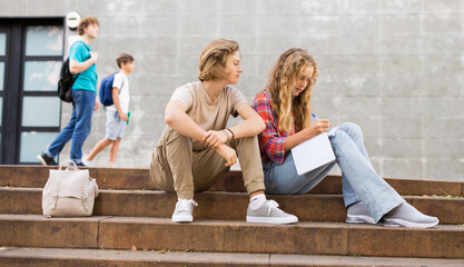 Guy helps girl to solve the school problem while sitting on stone stairs in front of the school