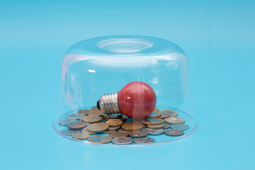 A red light bulb on top of a pile of coins in a glass safe