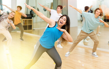 Naklejka na ściany i meble Cheerful emotional teen girl enjoying while training movements of modern group dance in choreography class .