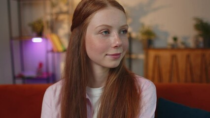 Close-up portrait of happy positive smiling young redhead child girl, looking at camera. Teen red-haired ginger freckles face kid indoor isolated at home in living room on couch. Female nature beauty