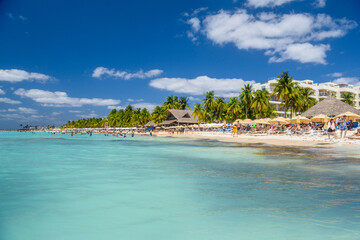 Fototapeta na wymiar People swimming near white sand beach with umbrellas, bungalow bar and cocos palms, turquoise caribbean sea, Isla Mujeres island, Caribbean Sea, Cancun, Yucatan, Mexico