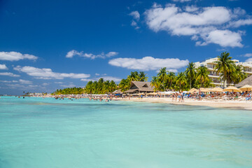 People swimming near white sand beach with umbrellas, bungalow bar and cocos palms, turquoise...